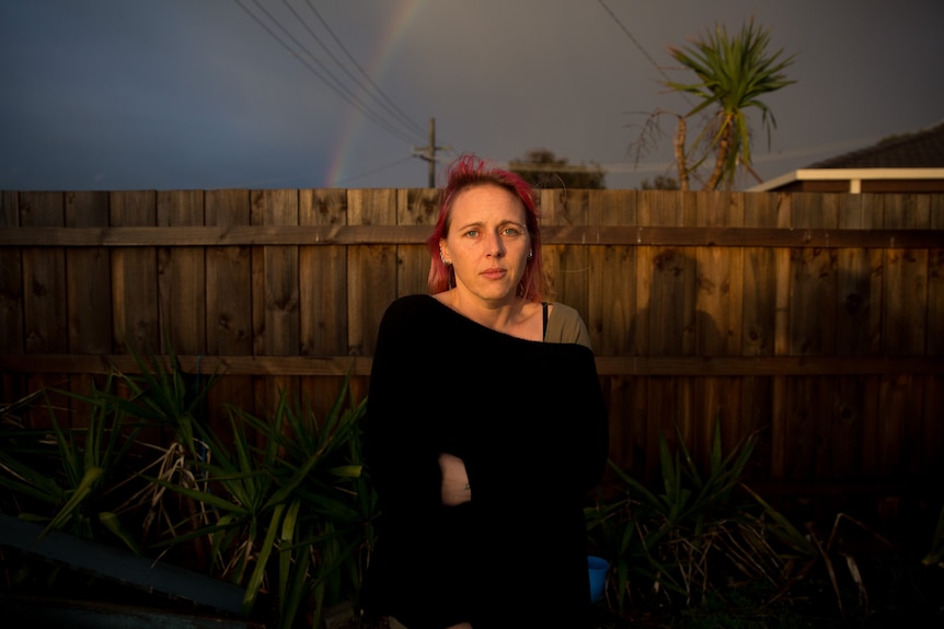 Amber stands in the backyard, with a rainbow in the background.