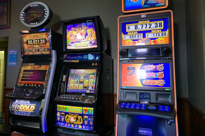Three poker machines lined up against a wall inside a venue