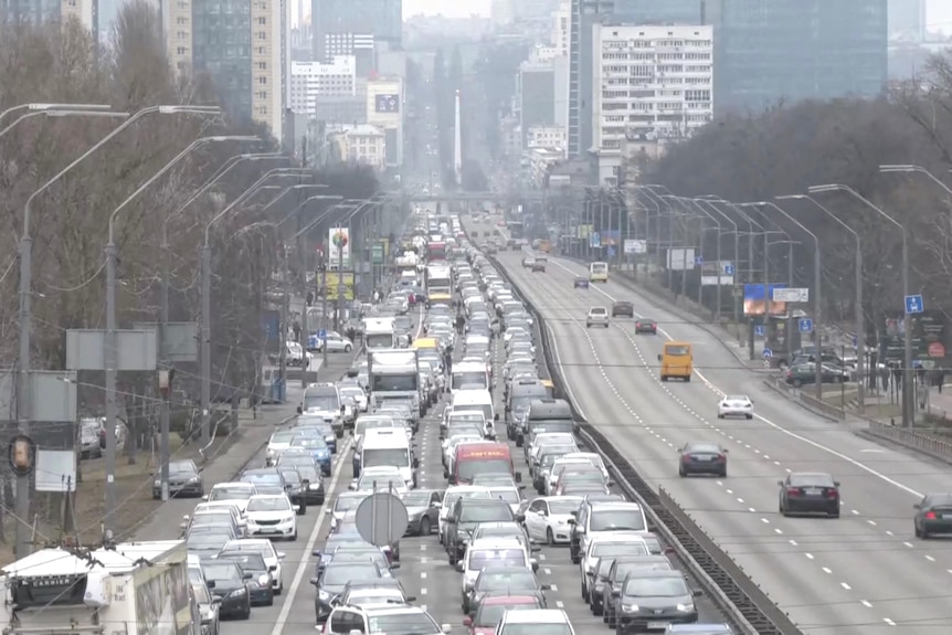 A long line of cars on a road out of a city.