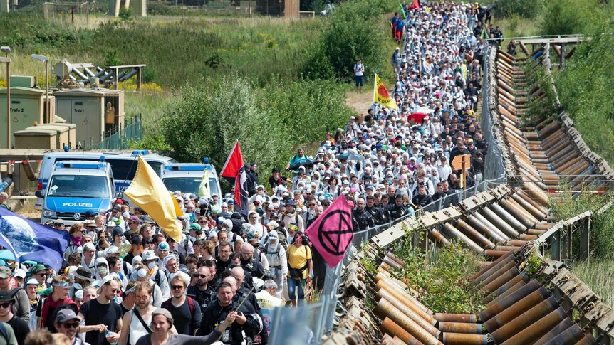 Hundreds of protesters walk along a railway track holding protest signs and peace flags.