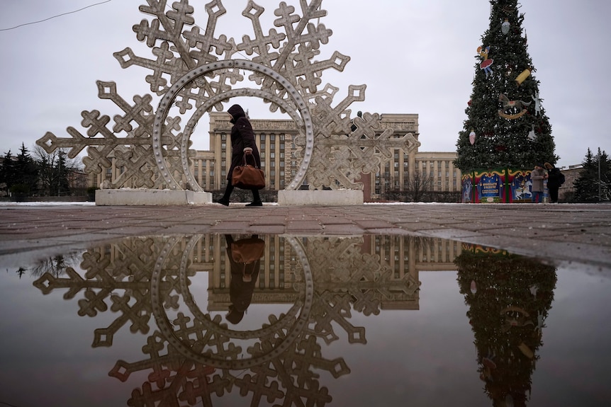 A woman walks by Christmas decorations in an outdoor square. 