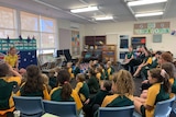 A woman in a primary classroom surrounded by students.