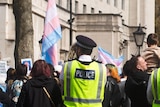police stand guard around a group of people waving trans pride flags