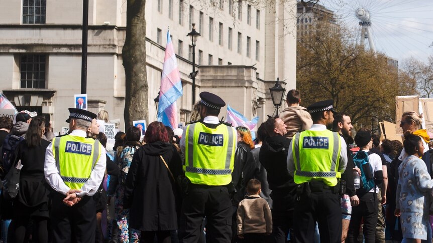 police stand guard around a group of people waving trans pride flags