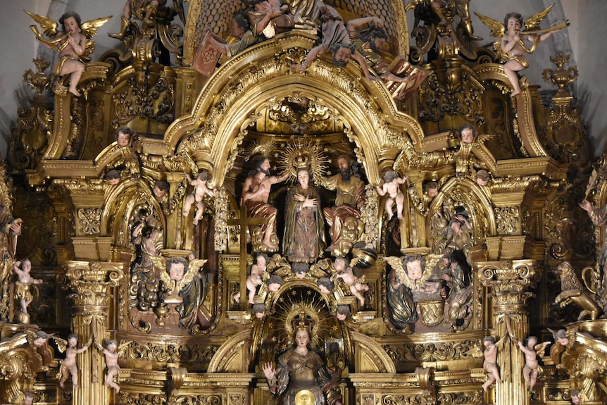 An elaborate gold sculpture depicts a coronation scene of the Catholic Virgin Mary surrounded by baby angels.