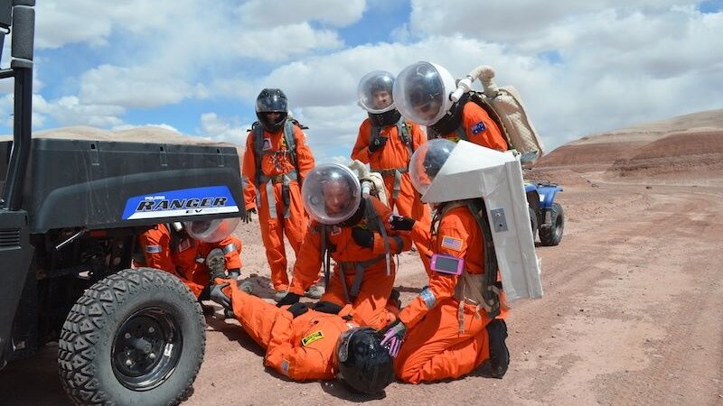 People in orange spacesuits simulate a medical emergency pretending to be on Mars