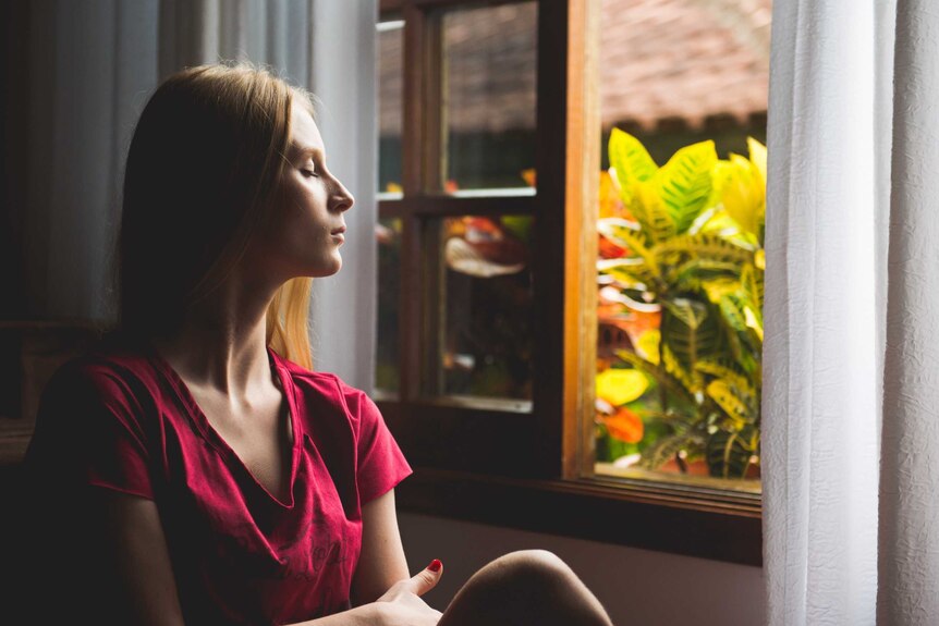 Woman sitting with eyes closed in front of a window for story about mindfulness techniques for coping with coronavirus stress.
