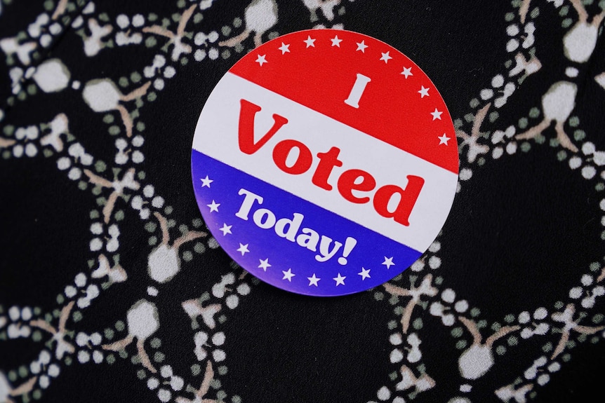 A red white and blue sticker saying "I voted today" pinned to some black, white, green and brown fabric