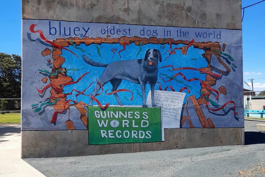 A blue mural on a brick wall depicting a smiling dog
