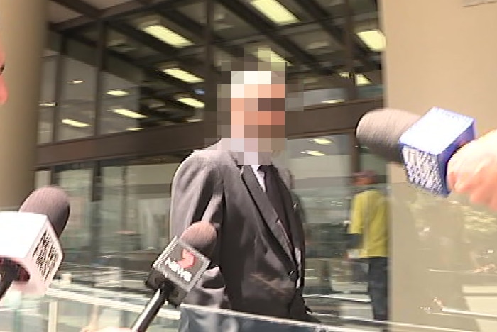 A man in a suit and sunglasses walks in front of a building.