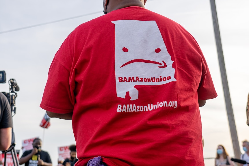 A man in a red shirt bearing an upside-down Amazon logo 