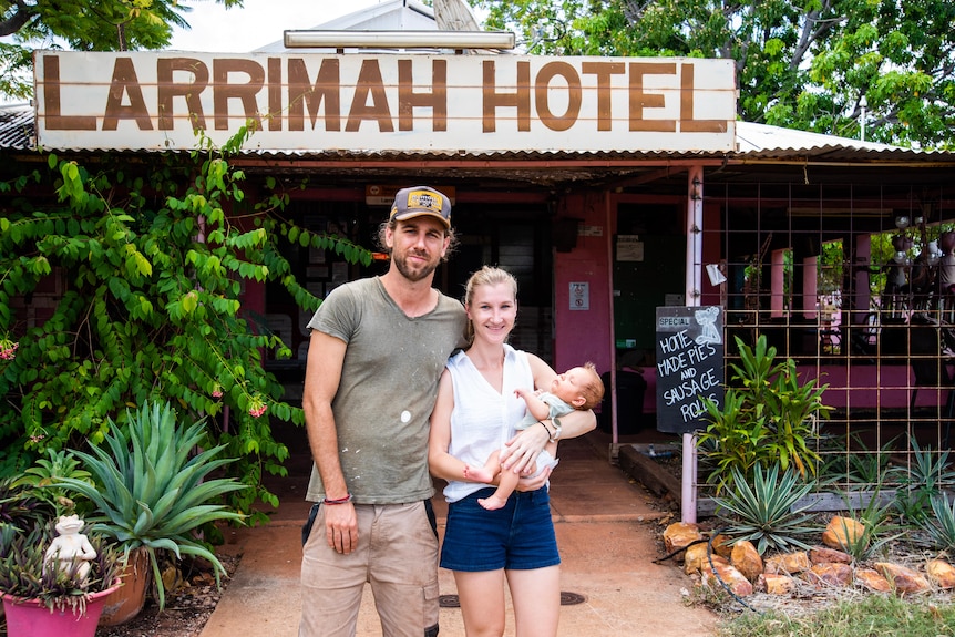 A couple with their new born baby stand in front of a hotel with a big sign saying Larrimah Hotel. 