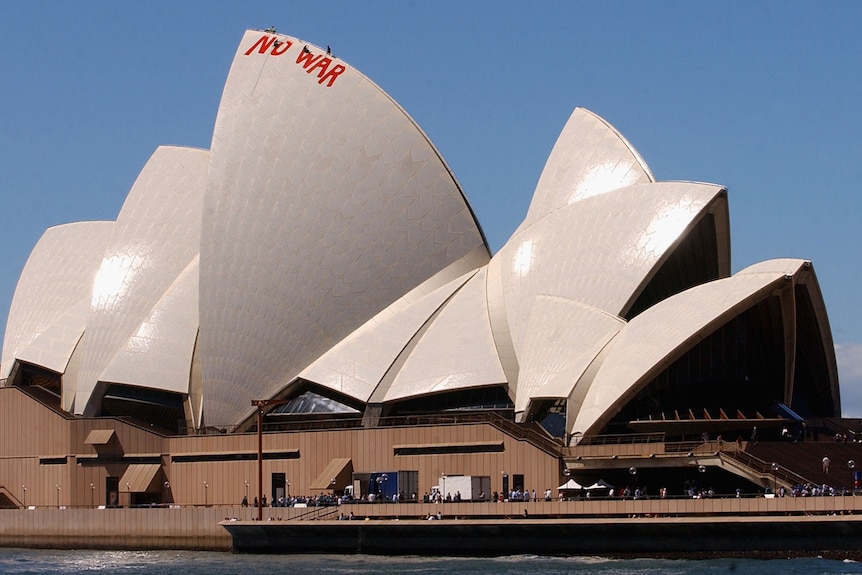 Men abseil from top of Opera House sail and begin to paint over the red NO WAR letters with white paint