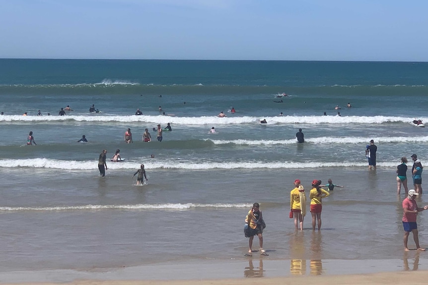 Swimmers in the water at a beach with two lifesavers looking on from the edge of the water.