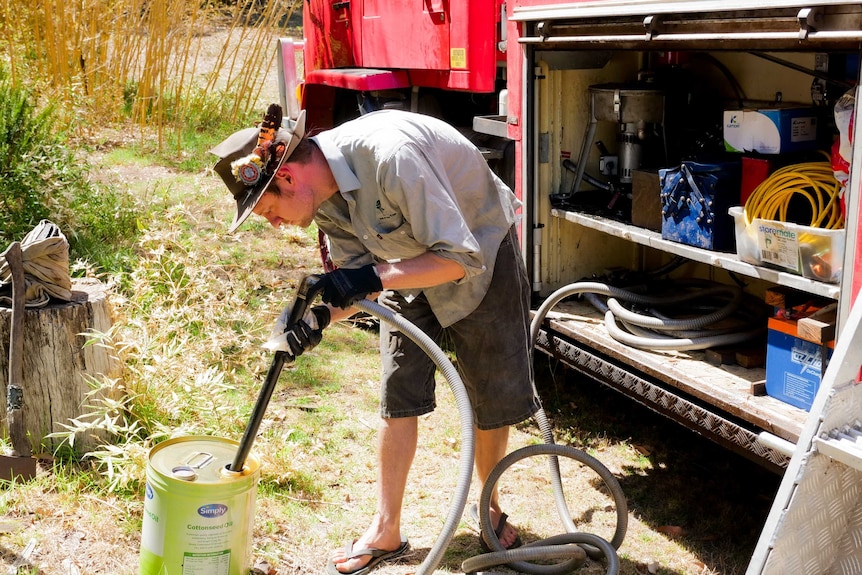 A man piping vegetable oil into the engine of a red truck.