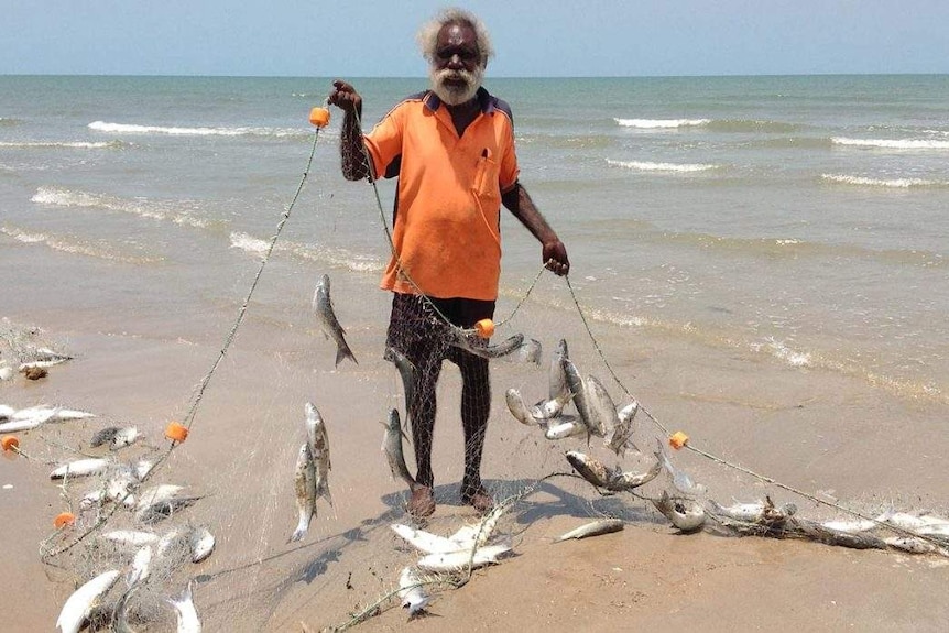 Don Wilton holding up a net with fish entangled on the shore.