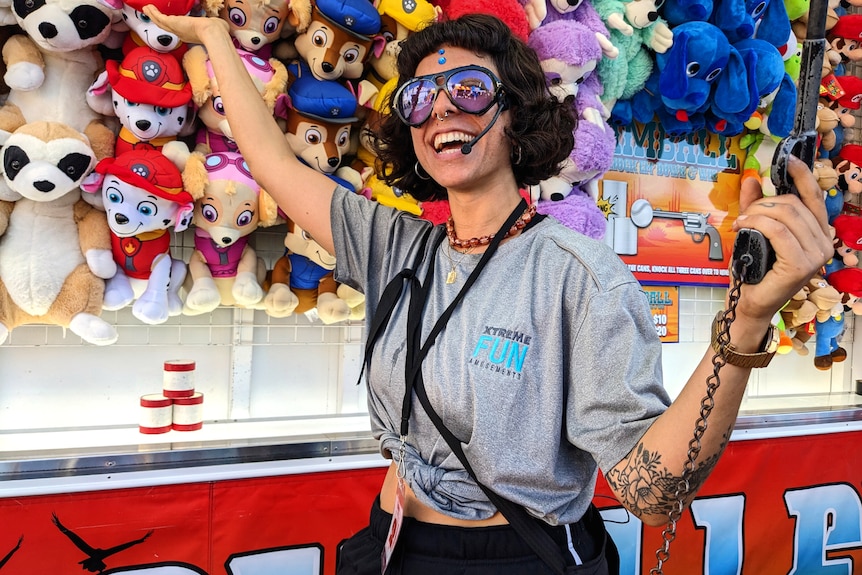 A trendy woman wearing sunglasses and a microphone headset gestures at a brightly coloured assortment of plush toy animals.
