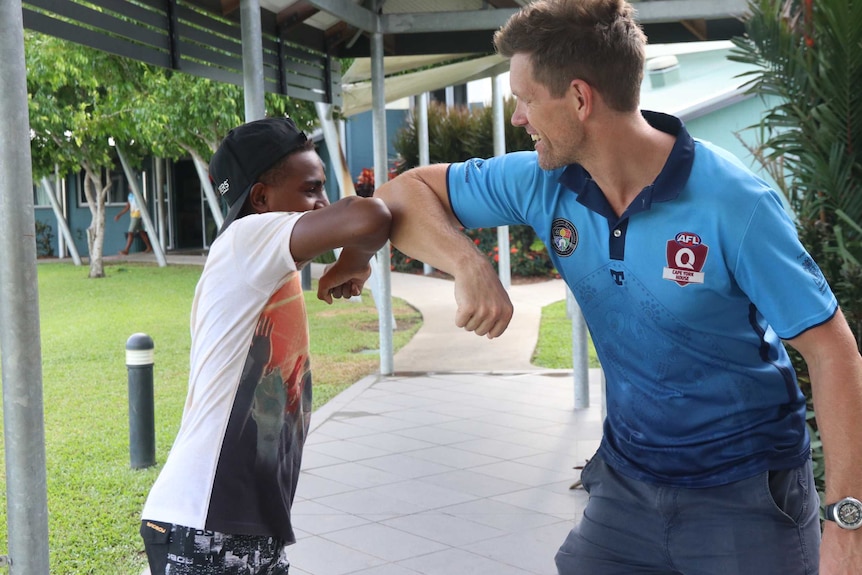 Young indigenous student and boarding house leader bump elbows in outside courtyard.