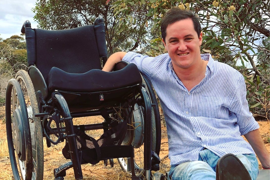 A man sits on the ground next to his wheelchair.