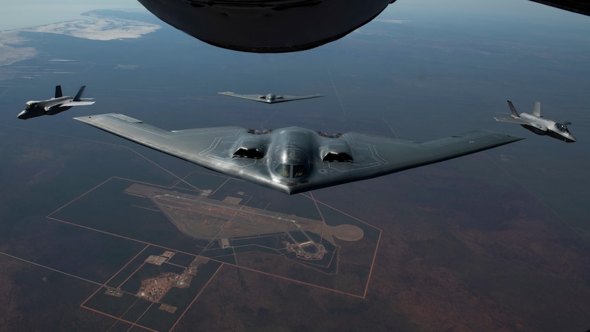 a flat triangle shaped black plane flies high over an airbase