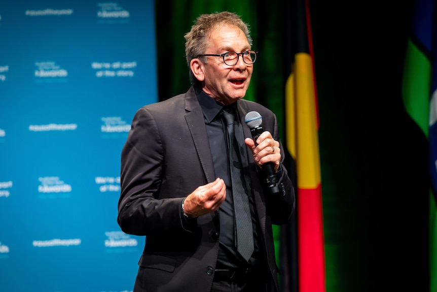 Man in suit on a stage with a microphone looking comfortable telling a story.