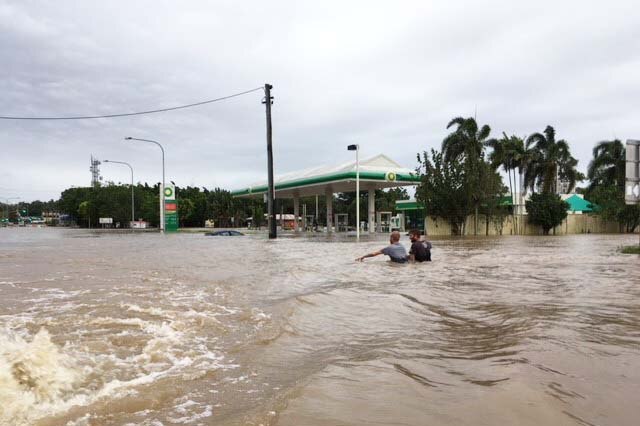 Two men wade through waist-deep floodwater on Townsville Road near the Bruce Highway in Ingham.