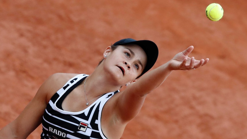 Ash Barty looks up as she throws a ball in the air with a red background