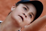 Ash Barty looks up as she throws a ball in the air with a red background