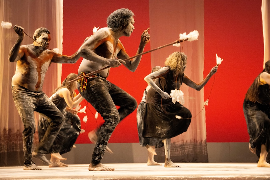 Dancers perform an ancient funeral ceremony on a red lit stage.