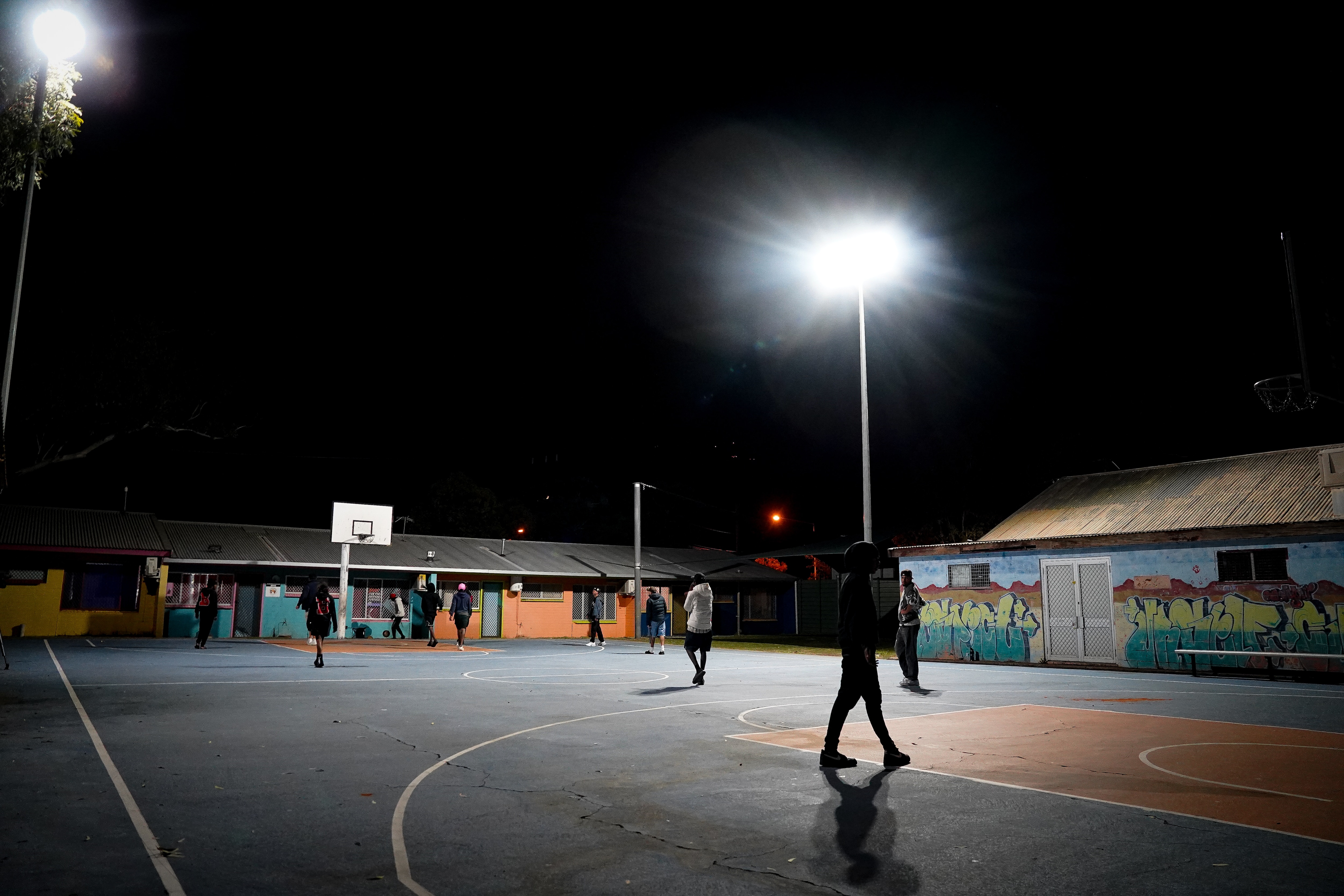 A group of unidentified teenagers on a basketball court at night.