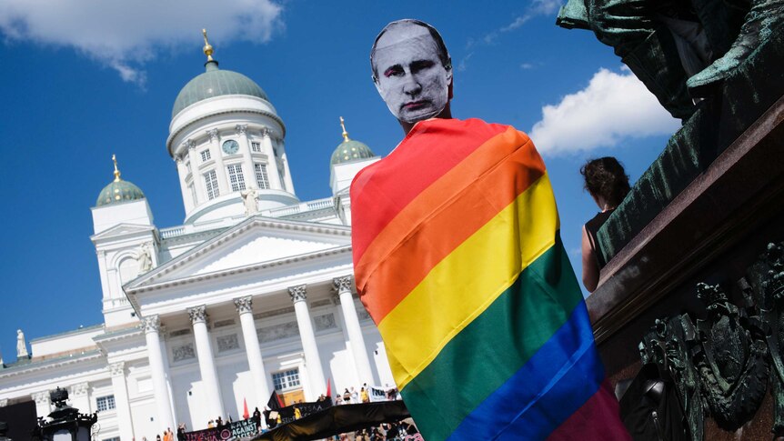 A man with a Putin mask and a rainbow flag attends a rally