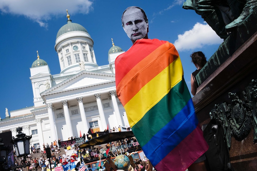 A man with a Putin mask and a rainbow flag attends a rally