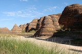 A group of stone mountains with sand and green grass in the foreground.