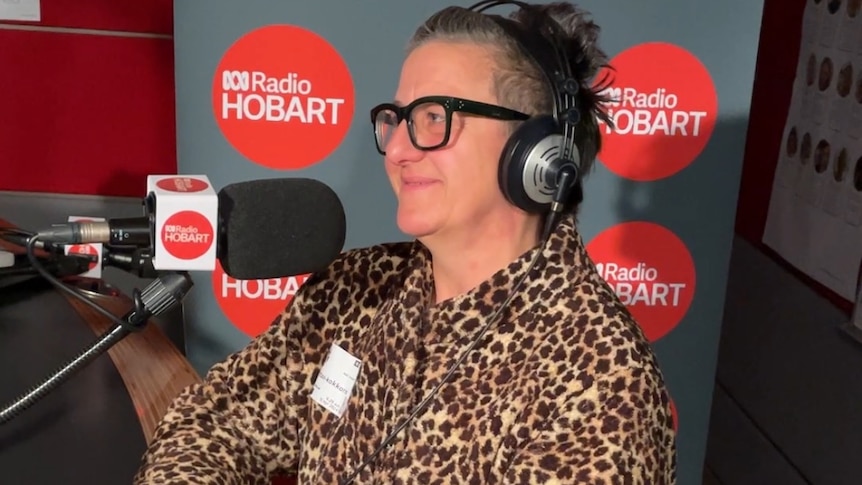 Rose has short grey hair, is wearing a large leopard-print coat and is sitting in front of a radio microphone.