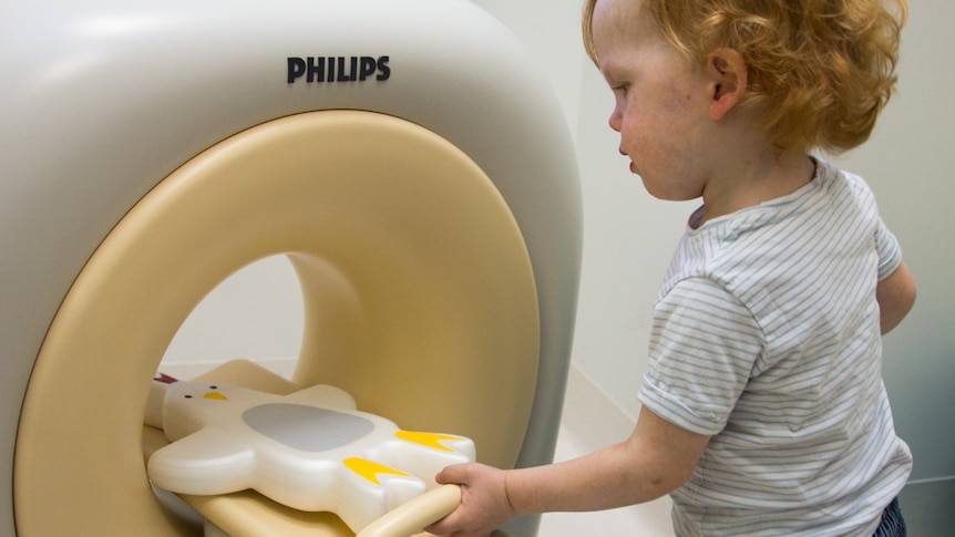 A young boy pushes a toy chicken on a tray into a circular white-and-beige device.