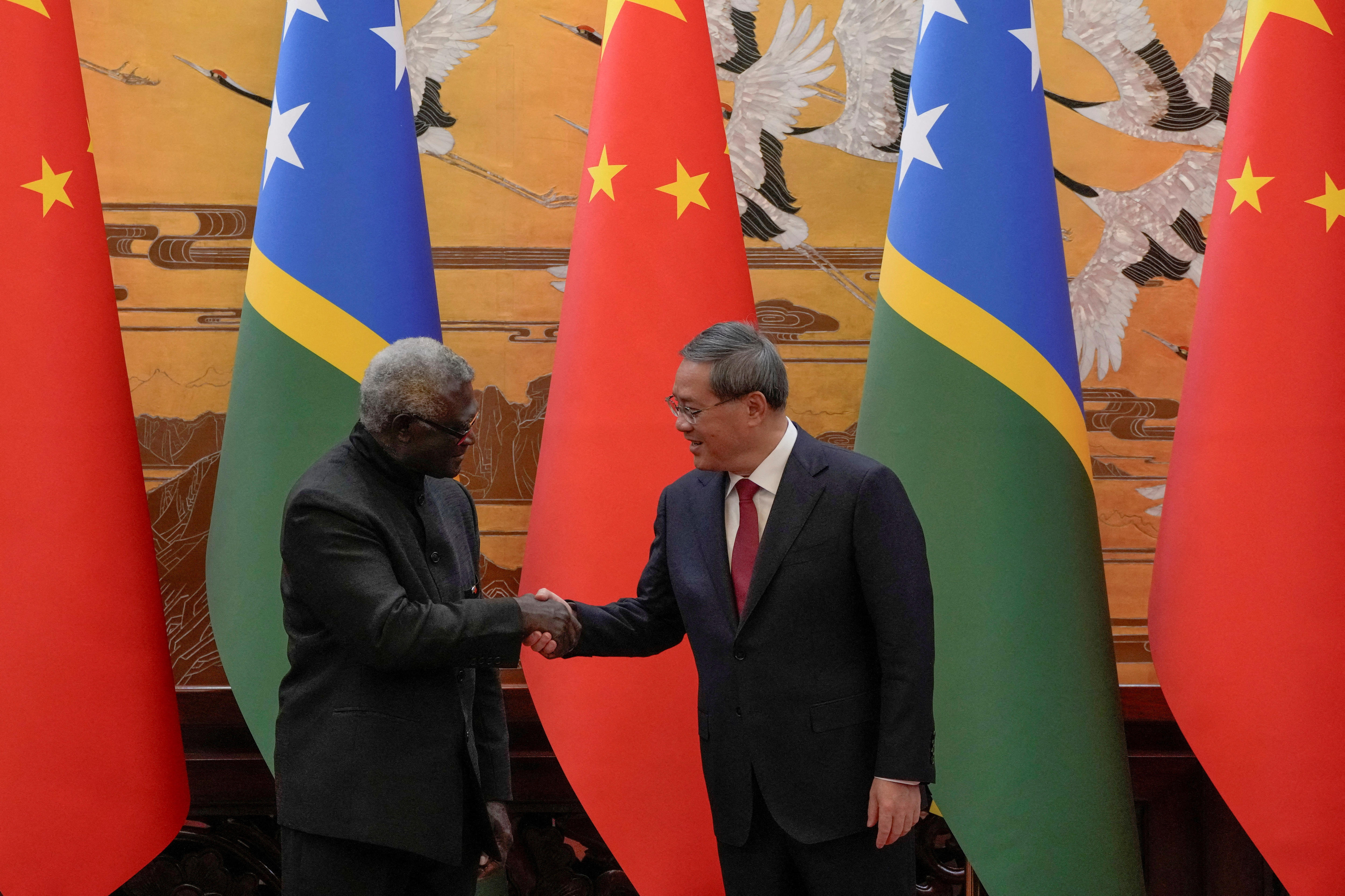Manasseh Sogavare shakes hands with his Chinese counterpart Li Qiang in front of flags from both of their countries.