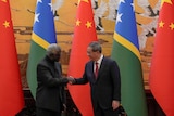Manasseh Sogavare shakes hands with his Chinese counterpart Li Qiang in front of flags from both of their countries.