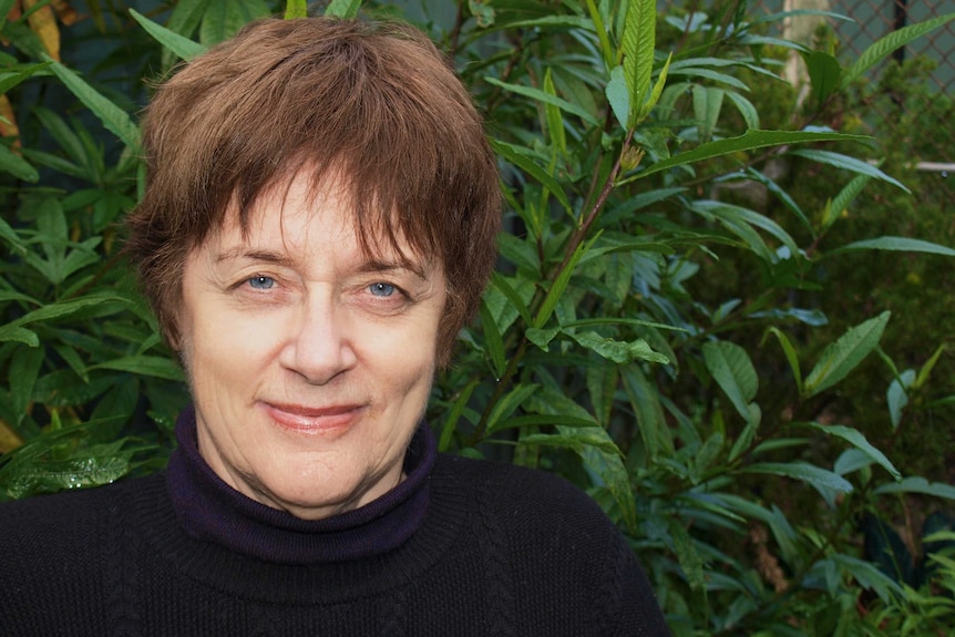 An older woman poses in front of a tree.