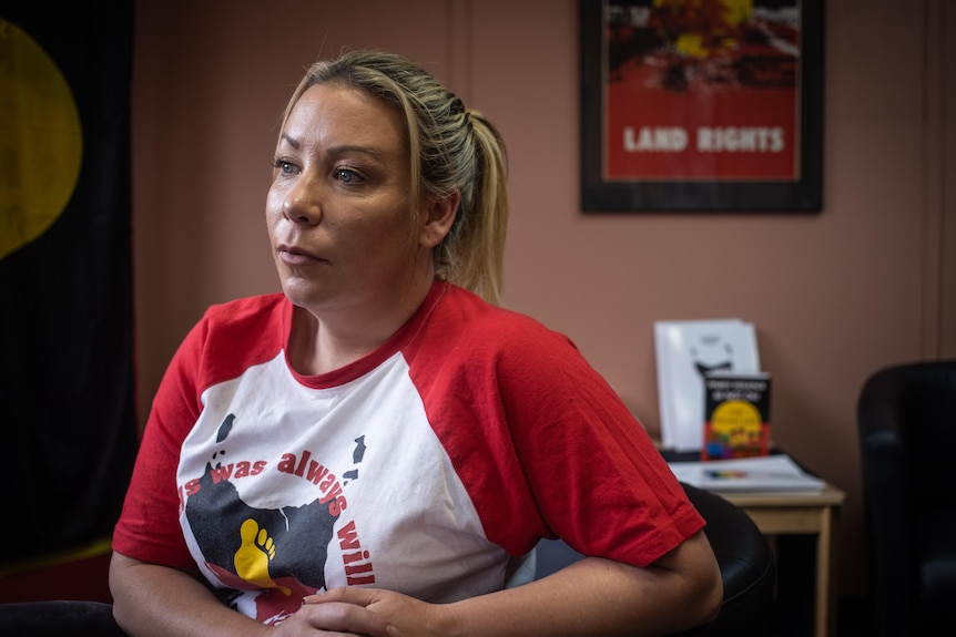 A woman wearing a t-shirt that says "always was, always will be" photographed looking away from the camera