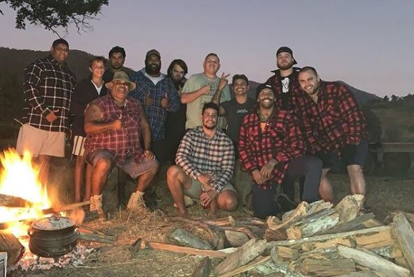 A group of 12 men in front of a camp fire