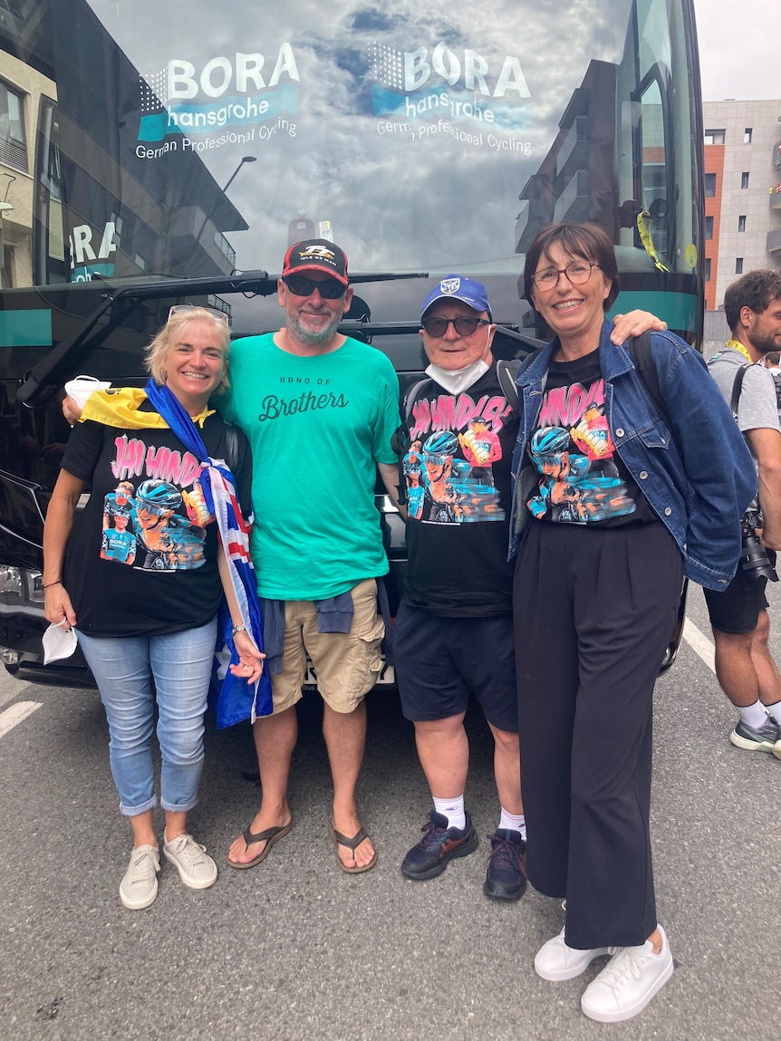 Four people stand in front of a team bus at the Tour de France, three of them wearing T-shirts saying 'Jai Hindley'.