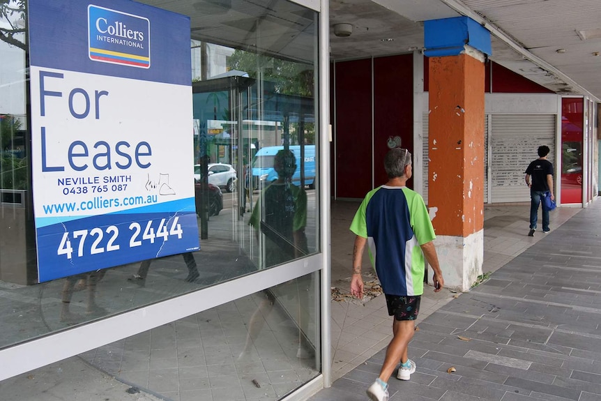 A man walks past an empty shop with a 'For Lease' sign.