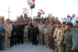Iraq's Prime Minister Haider al-Abadi raises the national flag as he addresses forces from a small base.