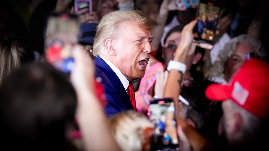 Donald Trump with his mouth open in a big crowd of people holding phones