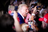 Donald Trump with his mouth open in a big crowd of people holding phones