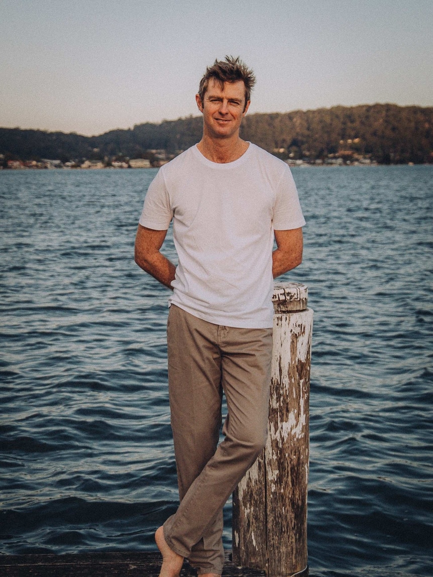 Man leans against a jetty post with water in the background