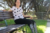 Lisa Burnette sits on a park bench smiling with her prosthetic legs visible below her knees.