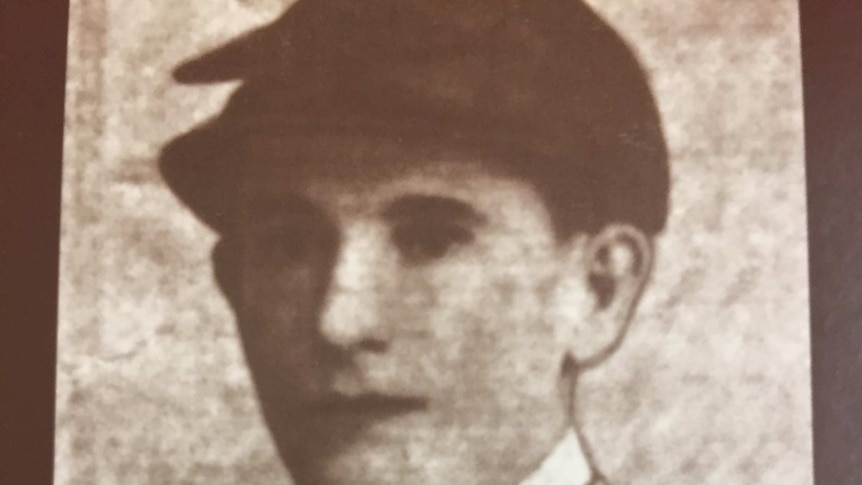 A black and white headshot of what appears to be a male jockey in uniform.