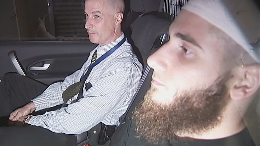 Agim Kruezi (right) sits in a police car.