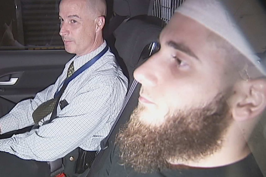 Agim Kruezi (right) sits in a police car.